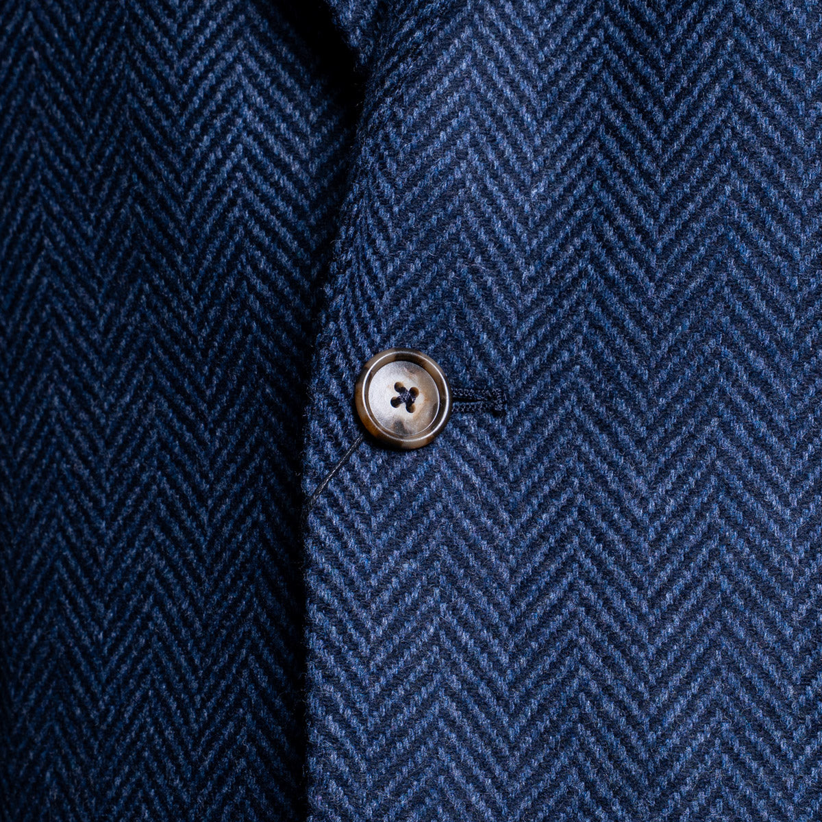 Close-up of a navy blue herringbone tweed fabric with a single metallic button on the front. Sand Copenhagen Blazer available at Sakks Menswear in Southampton.
