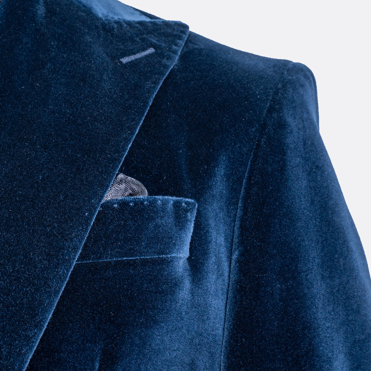 Close-up of a dark navy blue velvet blazer jacket with a pocket and a patterned pocket square, set against a plain white background. Sand Copenhagen Velvet Blazer available at Sakks Menswear in Southampton.