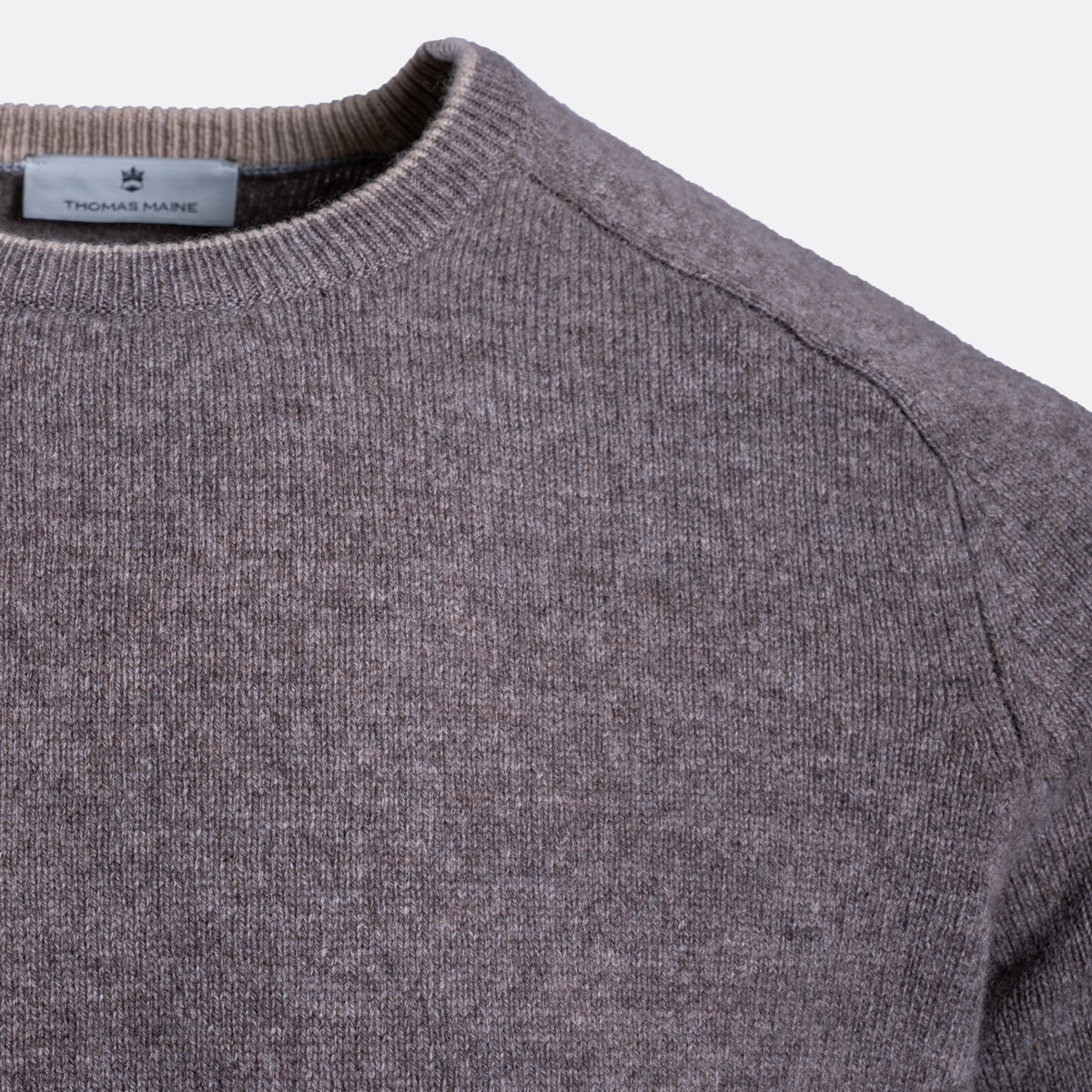 Close-up of a ribbed knit crewneck sweater in a heathered taupe-gray color, showing the inner neck label with the brand name 'Tweedmill'. Thomas Maine Jumper available at Sakks Menswear in Southampton.