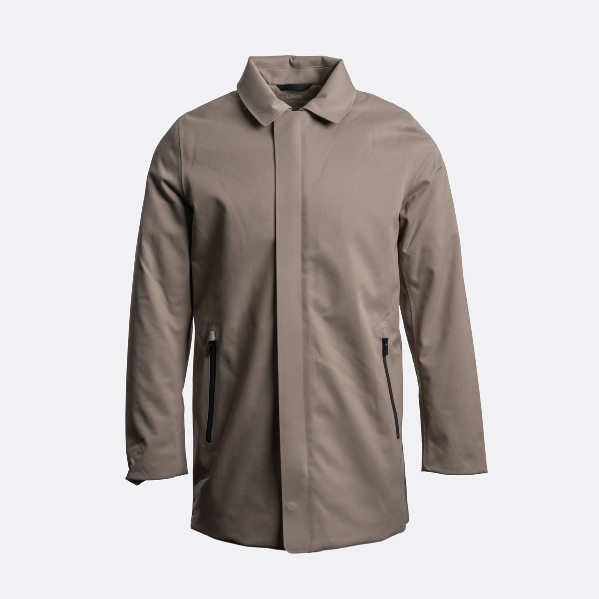A taupe-brown longline utility jacket with a pointed collar, front zipper closure, and zippered hand pockets, shown on a light gray background. UBR Jacket available at Sakks Menswear in Southampton.