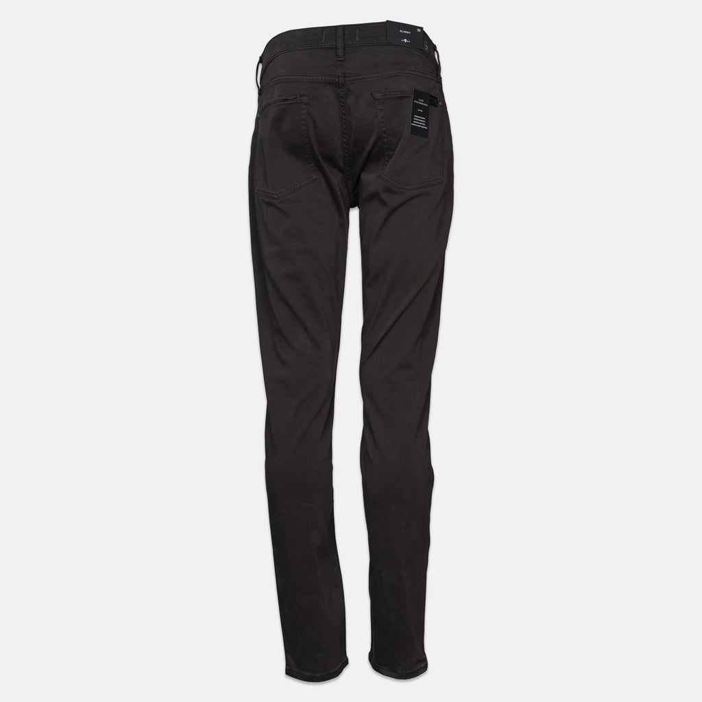 Black slim-fit jeans shown from the back, featuring a five-pocket design and a small black brand patch on the right pocket, set against a plain light gray background. 7 For All Mankind Chinos available at Sakks Menswear in Southampton.
