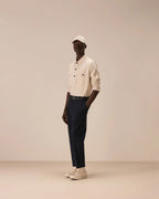 A model stands in profile wearing a cream-colored button-up shirt, dark navy trousers, a white cap, and off-white sneakers against a solid beige studio background. Circolo 1901 Sweatshirts available at Sakks Menswear in Southampton.
