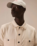 A man wearing a cream-colored collared button-up shirt and a matching cream baseball cap with red embroidered text, photographed against a solid beige background. Circolo 1901 Sweatshirts available at Sakks Menswear in Southampton.