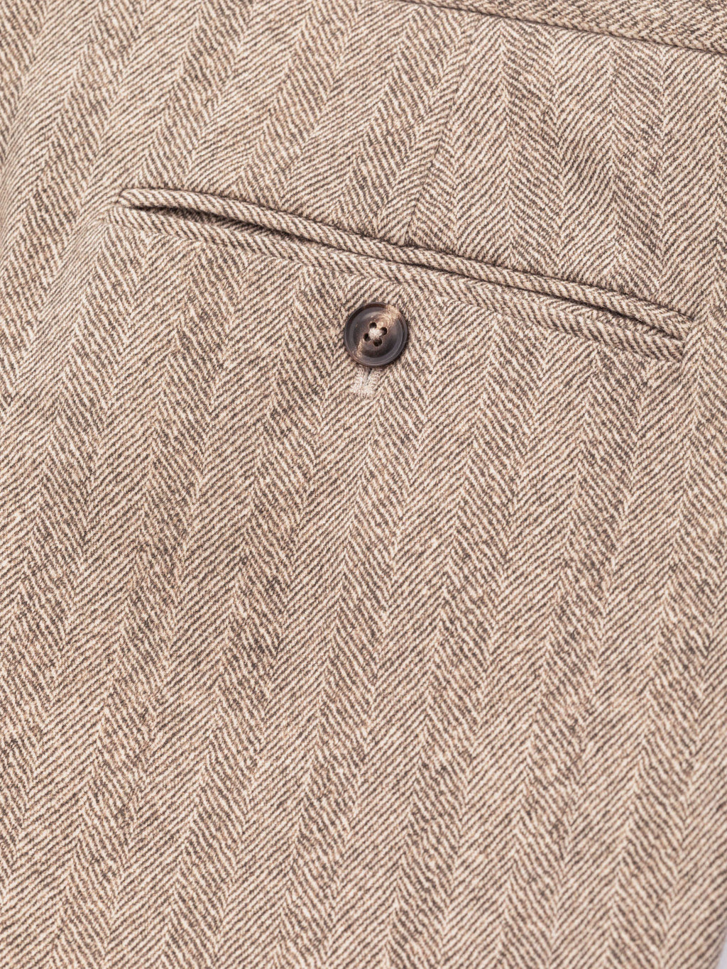 Close-up of a beige and brown herringbone tweed fabric with a single dark button and a stitched seam detail. Circolo 1901 Trousers available at Sakks Menswear in Southampton.