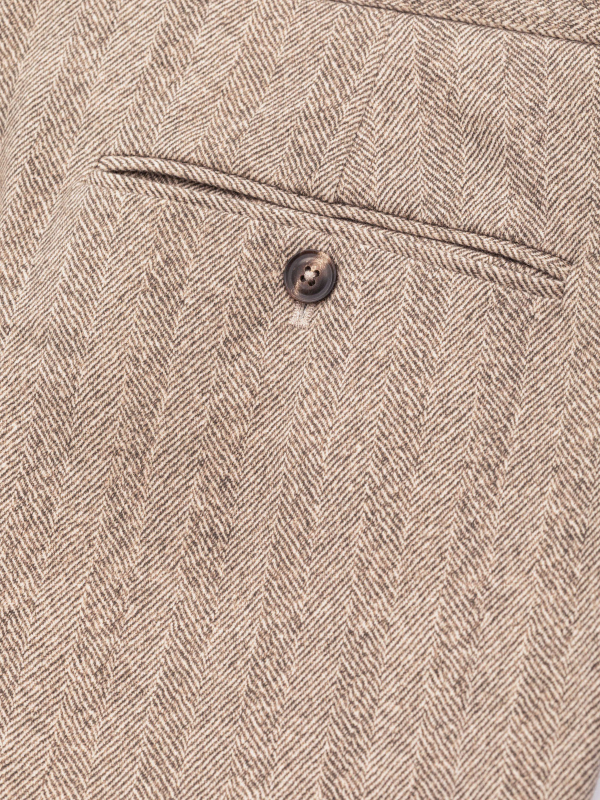 Close-up of a beige and brown herringbone tweed fabric with a single dark button and a stitched seam detail. Circolo 1901 Trousers available at Sakks Menswear in Southampton.