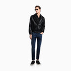 A male model wearing a black leather jacket, dark blue jeans, black sneakers, and sunglasses, standing against a solid white background. Emporio Armani Jeans available at Sakks Menswear in Southampton.