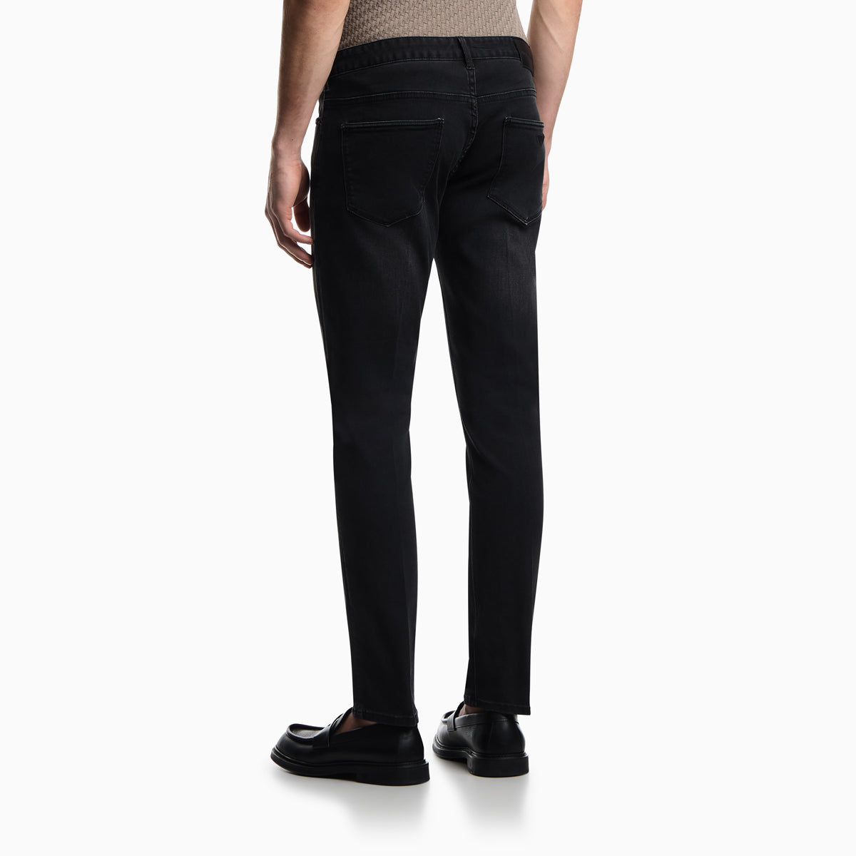Rear view of a person wearing slim black jeans and black loafers against a clean white studio background. Emporio Armani Jeans available at Sakks Menswear in Southampton.