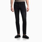 A model wearing slim-fit black jeans, a beige patterned knit top, and black leather loafers, shown from the waist down on a clean white studio background. Emporio Armani Jeans available at Sakks Menswear in Southampton.