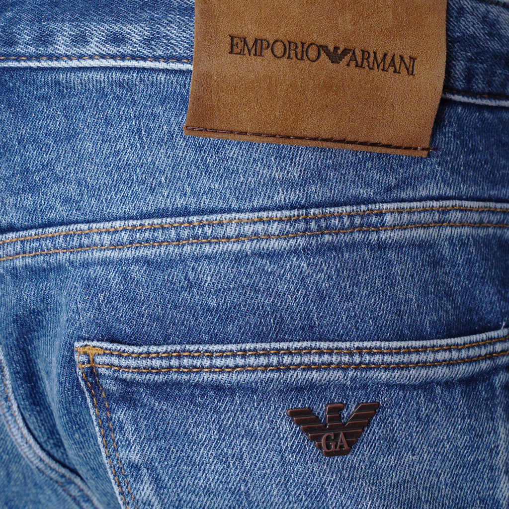 Close-up of blue denim jeans showing the back pocket, brown leather brand patch with 'EMPORIO ARMANI' text, and the dark brown embroidered eagle logo. Emporio Armani Jeans Available at Sakks Menswear in Southampton.