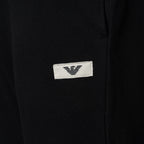 Close-up of a black textured fabric garment featuring a small white rectangular patch with the black embroidered Emporio Armani eagle logo. Emporio Armani Joggers available at Sakks Menswear in Southampton.