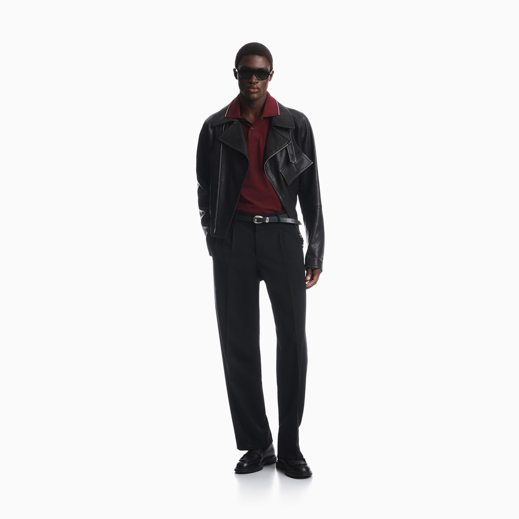 A model stands against a plain white studio background wearing a black leather jacket, black trousers, a dark red collared shirt, a black belt, and black loafers. Emporio Armani Polo available at Sakks Menswear in Southampton