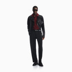 A model stands against a plain white studio background wearing a black leather jacket, black trousers, a dark red collared shirt, a black belt, and black loafers. Emporio Armani Polo available at Sakks Menswear in Southampton