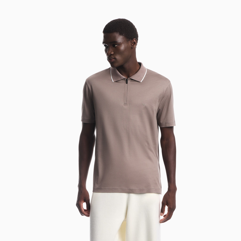 A man wearing a taupe brown short-sleeve polo shirt with a white-trimmed collar and a half-zip neckline, paired with off-white trousers, against a plain white background. Emporio Armani olo available at Sakks Menswear in Southampton.