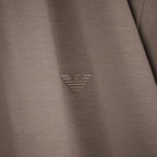 Close-up of a taupe-brown textured fabric with a small metallic silver embroidered logo in the center. Emporio Armani olo available at Sakks Menswear in Southampton.