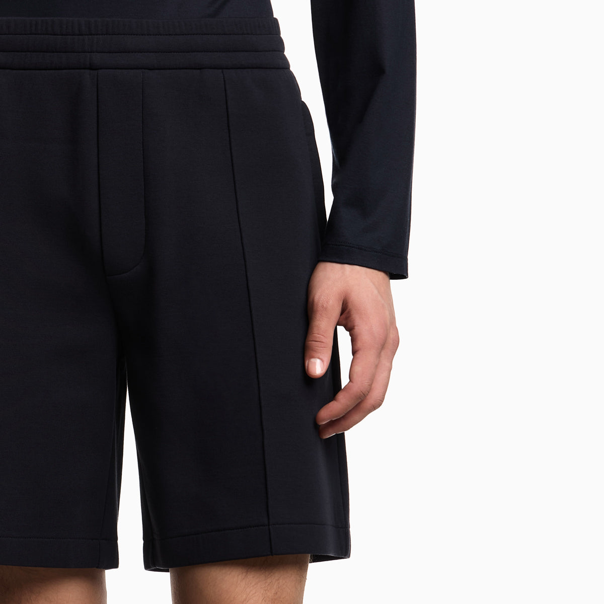 Close-up of a person wearing black pleated athletic shorts with a matching black long-sleeve top, shown against a plain white background. Emporio Armani Shorts available at Sakks Menswear in Southampton.