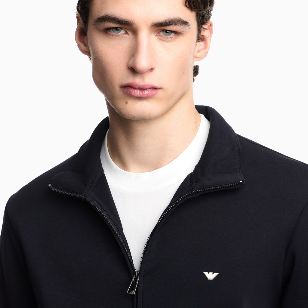 Man wearing a black jacket with a logo on a white background. Emporio Armani Sweatshirt available at Sakks Menswear in Southampton.