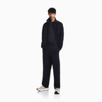 A male model stands in a studio wearing a dark navy blue jacket, matching sweatshirt, and trousers, paired with light gray sneakers, against a solid white background. Emporio Armani Jacket available at Sakks Menswear in Southampton.