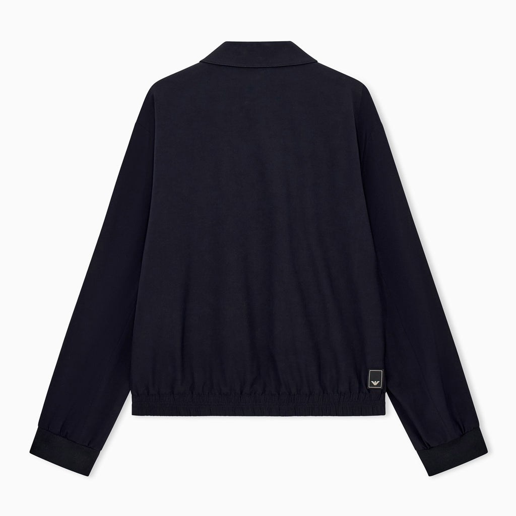 A dark navy blue jacket shown from the back, featuring a short stand collar, long sleeves with ribbed cuffs, and a small rectangular brand patch near the lower right hem, set against a plain white background. Emporio Armani Jacket available at Sakks Menswear in Southampton.