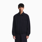 A man wearing a dark navy zip-up jacket with a collar and elastic cuffs, standing against a plain white background. Emporio Armani Jacket available at Sakks Menswear in Southampton.