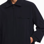 A close-up of a person wearing a dark navy zip-front jacket with a collar and a zippered chest pocket, shown against a plain white background. Emporio Armani Jacket available at Sakks Menswear in Southampton.
