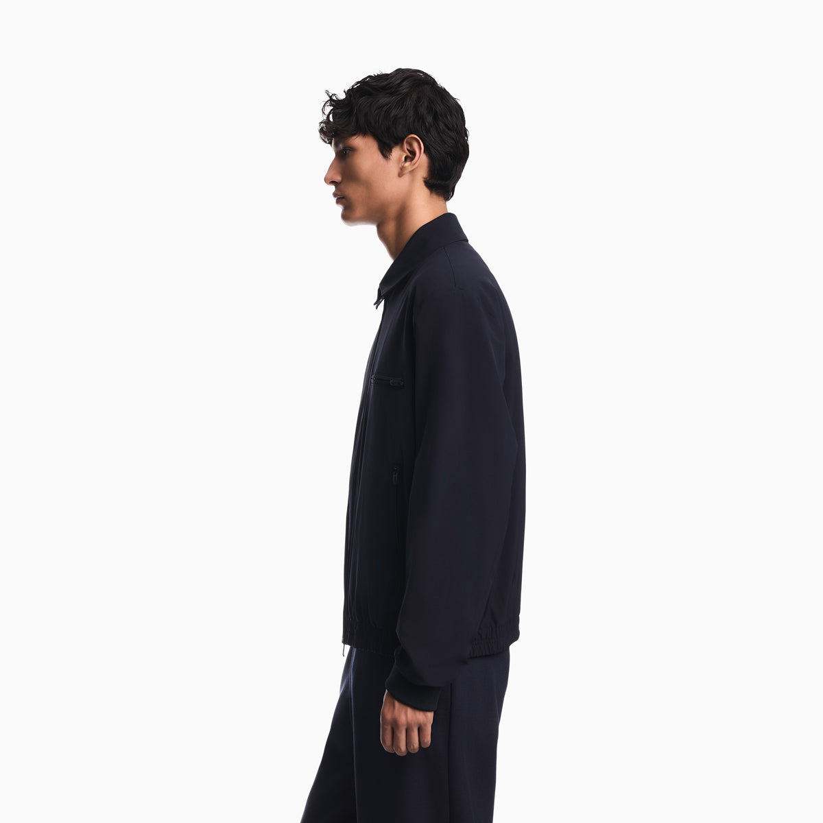 A man in profile wearing a dark navy long-sleeve jacket and matching dark pants, photographed against a clean white studio background. Emporio Armani Jacket available at Sakks Menswear in Southampton.