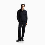 A model stands against a plain white studio background wearing a dark navy quilted zip-up jacket, matching dark trousers, and black shoes. Emporio Armani Down Jacket available at Sakks Menswear in Southampton.