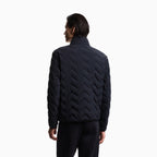 A man viewed from the back wearing a dark navy quilted puffer jacket with a distinctive chevron pattern and black pants, set against a plain white studio background. Emporio Armani Down Jacket available at Sakks Menswear in Southampton.