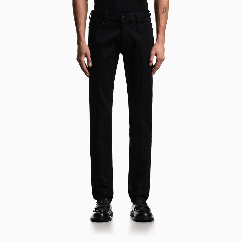 A model from the waist down wearing black slim-fit jeans and black leather shoes, photographed against a clean white studio background. Emporio Armani Jeans available at Sakks Menswear in Southampton.