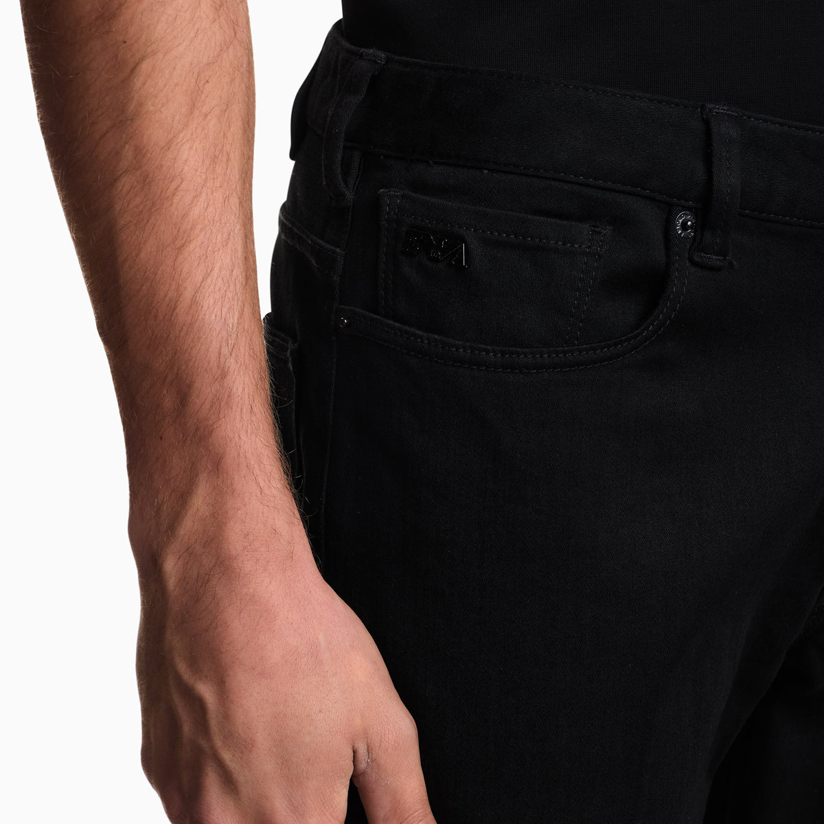 Close-up of a person wearing black denim jeans, showing the back pocket and waistband area against a plain white background. Emporio Armani Jeans available at Sakks Menswear in Southampton.