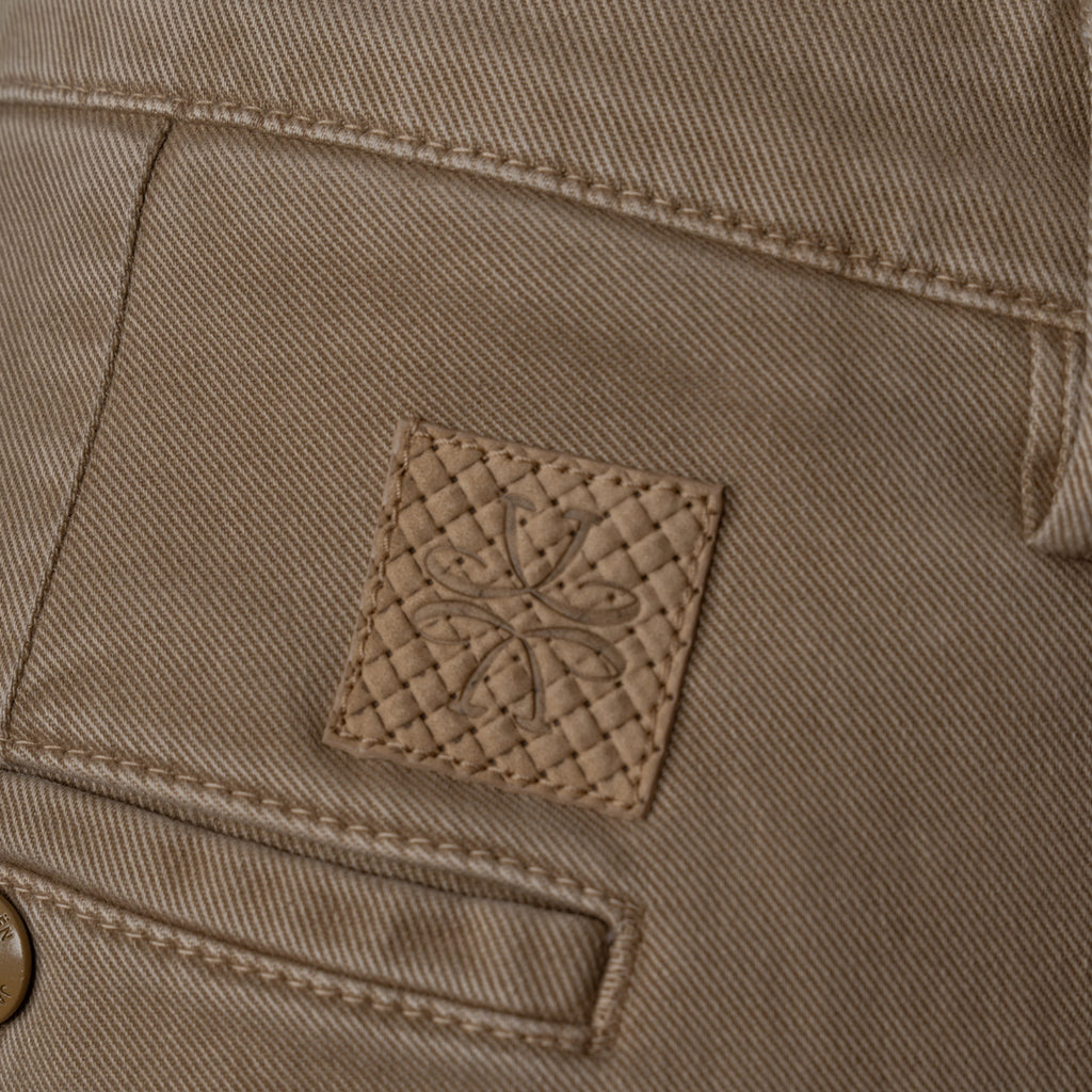 Close-up of a tan denim fabric with a small square quilted leather patch featuring an embossed floral design. Jacob Cohen Jeans available at Sakks Menswear in Southampton.