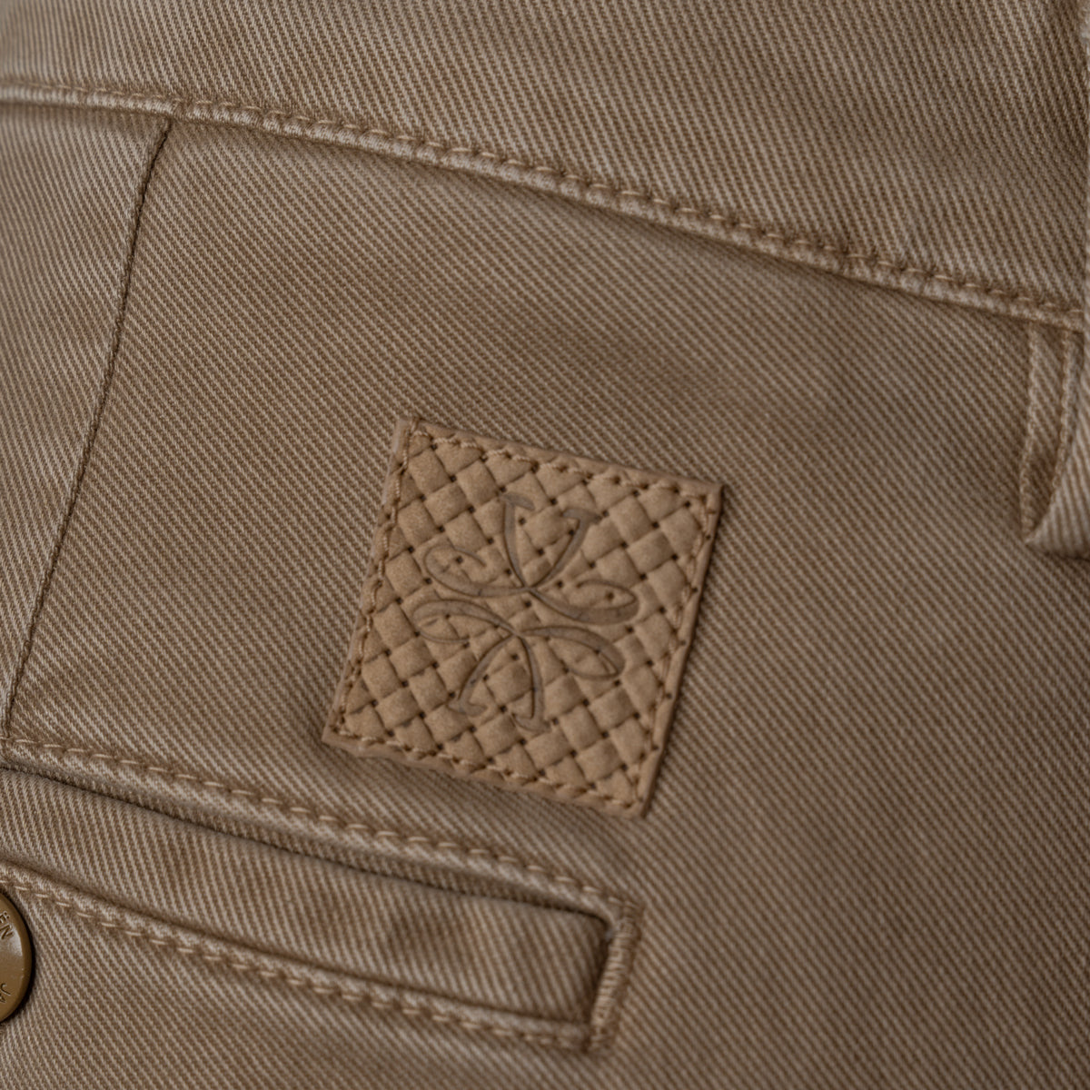 Close-up of a tan denim fabric with a small square quilted leather patch featuring an embossed floral design. Jacob Cohen Jeans available at Sakks Menswear in Southampton.