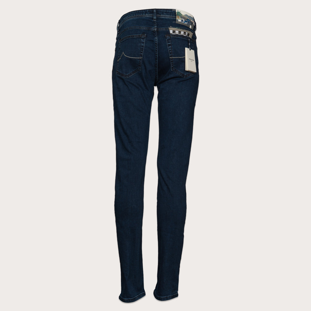 Back view of dark blue slim-fit jeans with a white paper tag attached to the back pocket, displayed on a light beige background. Jacob Cohen Jeans available at Sakks Menswear in Southampton.