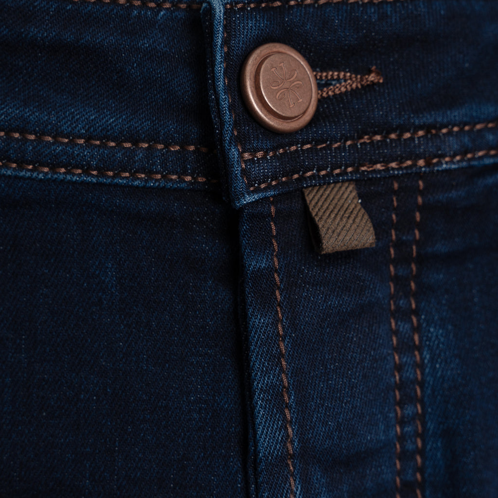 Close-up of dark blue denim jeans showing the button closure, contrast stitching, and a small fabric brand tab. Jacob Cohen Jeans available at Sakks Menswear in Southampton.