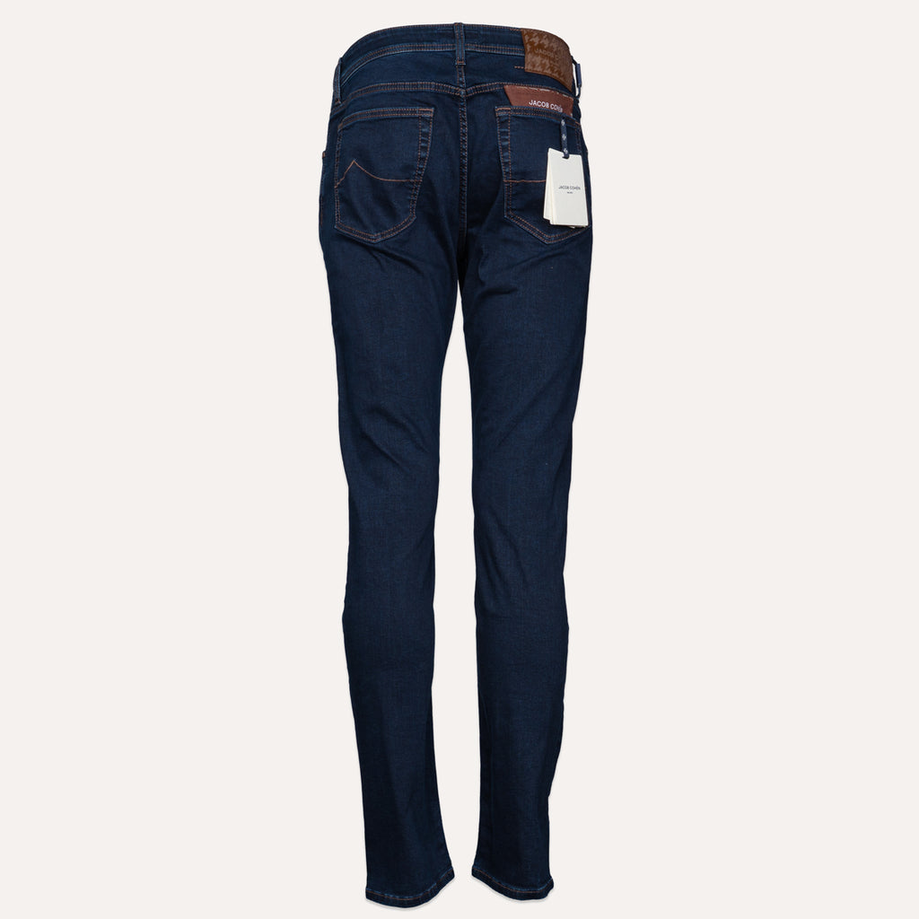 Back view of a pair of dark blue denim jeans on a light beige background, showing the back pockets, belt loops, and a white product tag. Jacob Cohen Jeans available at Sakks Menswear in Southampton.