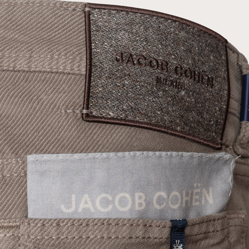 Close-up of the waistband of a pair of Jacob Cohen trousers, showing a textured dark brown brand patch and a light gray fabric label. Jacob Cohen Trousers available at Sakks Menswear in Southampton.