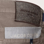 Close-up of the waistband of a pair of Jacob Cohen trousers, showing a textured dark brown brand patch and a light gray fabric label. Jacob Cohen Trousers available at Sakks Menswear in Southampton.