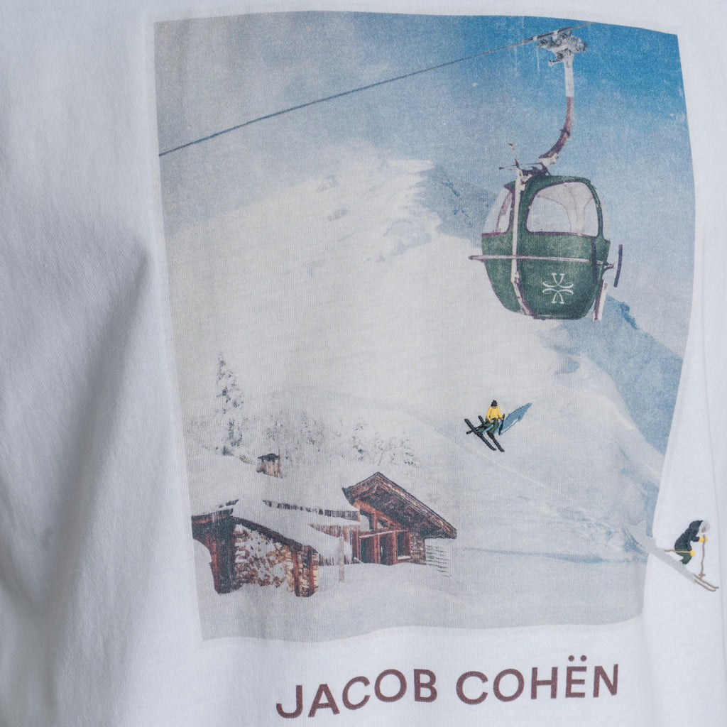 A close-up of a white graphic t-shirt featuring a vintage-style ski resort print with a gondola, skier, and chalets, with the brand name 'JACOB COHËN' printed below. Jacob Cohen T-Shirt available at Sakks Menswear in Southampton.