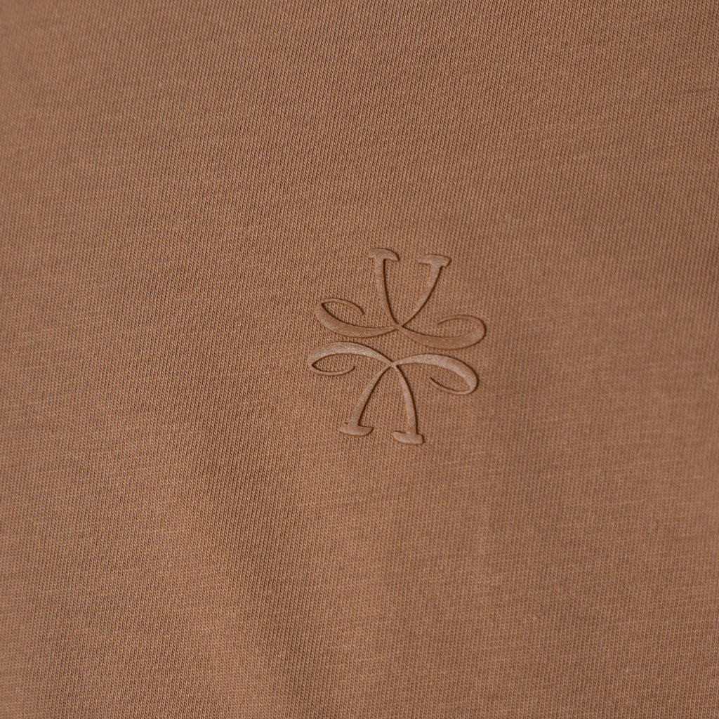 Close-up of a brown ribbed knit fabric with a tonal embroidered logo in the center. Jacob Cohen T-Shirt available at Sakks Menswear in Southampton.