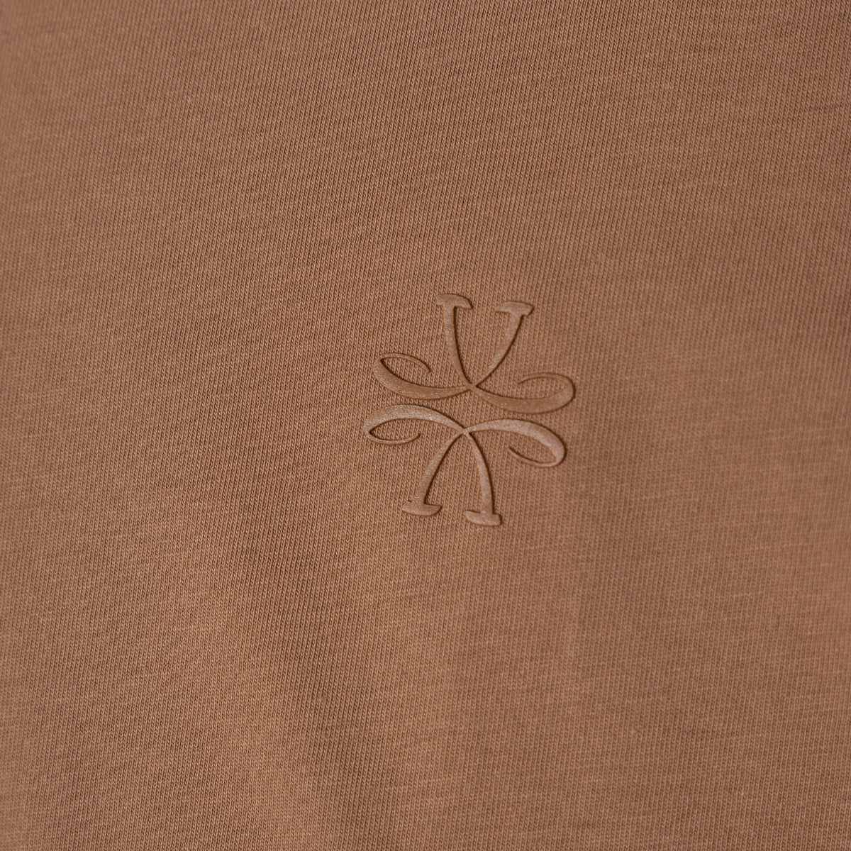 Close-up of a brown ribbed knit fabric with a tonal embroidered logo in the center. Jacob Cohen T-Shirt available at Sakks Menswear in Southampton.
