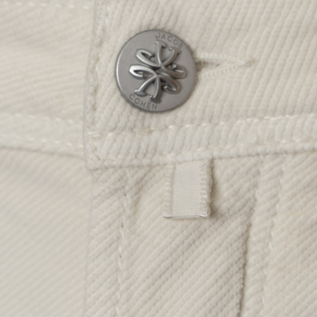 Close-up of a cream-colored textured fabric garment featuring a silver-tone metal button with the engraved brand name 'JACOB COHEN' and a matching fabric tab. Jacob Cohen Jeans available at Sakks Menswear in Southampton.