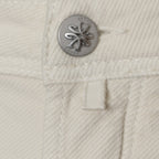 Close-up of a cream-colored textured fabric garment featuring a silver-tone metal button with the engraved brand name 'JACOB COHEN' and a matching fabric tab. Jacob Cohen Jeans available at Sakks Menswear in Southampton.