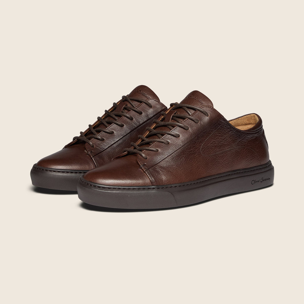 Brown cup sole sneakers in front of a light beige background.  Oliver Sweeney Shoes are available at Sakks Menswear in Southampton.