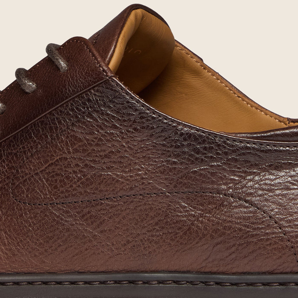 Close-up of a dark brown textured leather shoe with dark gray laces and a tan interior lining, shown against a light beige background. Oliver Sweeney Shoes are available at Sakks Menswear in Southampton.