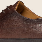 Close-up of a dark brown textured leather shoe with dark gray laces and a tan interior lining, shown against a light beige background. Oliver Sweeney Shoes are available at Sakks Menswear in Southampton.