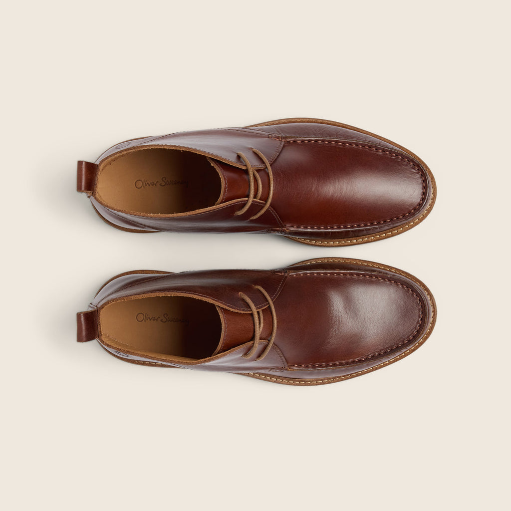 A pair of brown leather lace-up chukka boots shown from a top-down view on a light beige background. The brand name 'Oliver Sweeney' is visible on the insoles. Oliver Sweeney Moccasin Boots Available at Sakks Menswear in Southampton.