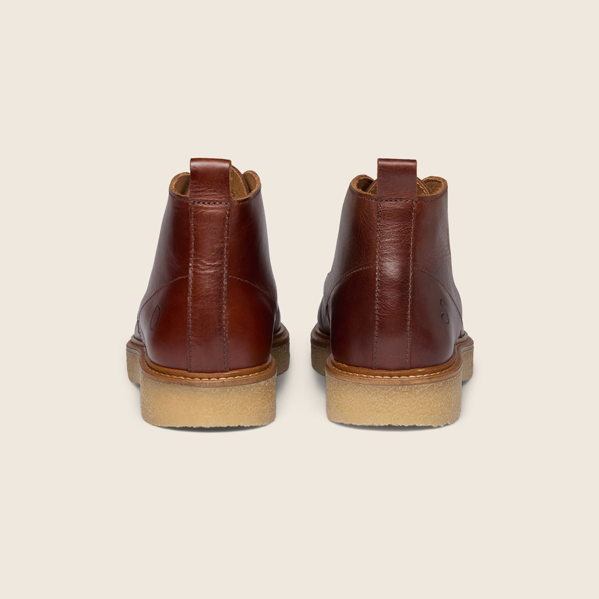 A pair of brown leather ankle boots shown from the back, featuring a tan rubber sole, set against a solid light beige background. Oliver Sweeney Moccasin Boots Available at Sakks Menswear in Southampton.