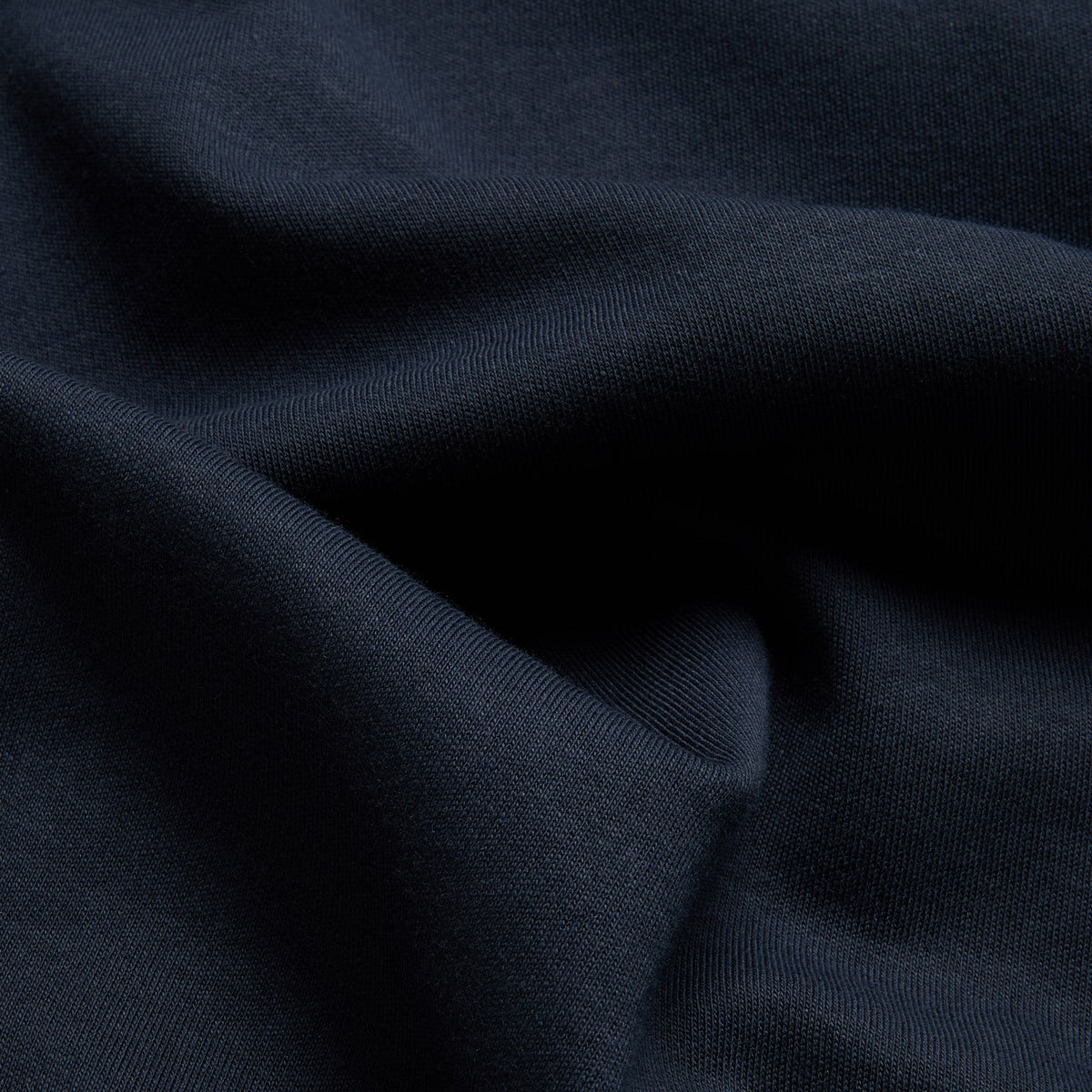 A close-up of dark navy blue fabric with soft folds and a fine ribbed texture. Oliver Sweeney T-Shirts available at Sakks Menswear in Southampton.