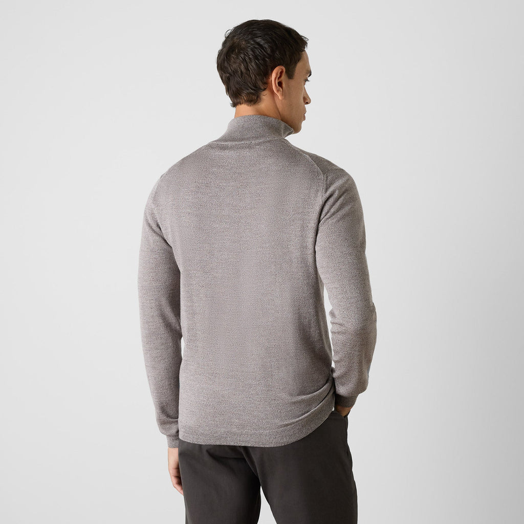 A man viewed from the back wearing a light gray ribbed mock neck sweater and dark gray pants, standing against a light gray studio background. Oliver Sweeney Sweater available at Sakks Menswear in Southampton.