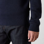 Close-up of a person wearing a dark navy ribbed knit sweater with dark denim jeans, showing the sleeve cuff and hand against a light gray background. Oliver Sweeney Sweater available at Sakks Menswear in Southampton.