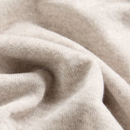 A close-up of draped knit fabric in a light warm off-white or cream tone, showing the texture and folds of the material. Oliver Sweeney knitwear available at Sakks Menswear in Southampton.